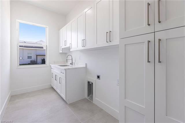 Laundry room featuring hookup for an electric dryer, baseboards, a sink, light tile patterned flooring, and cabinet space
