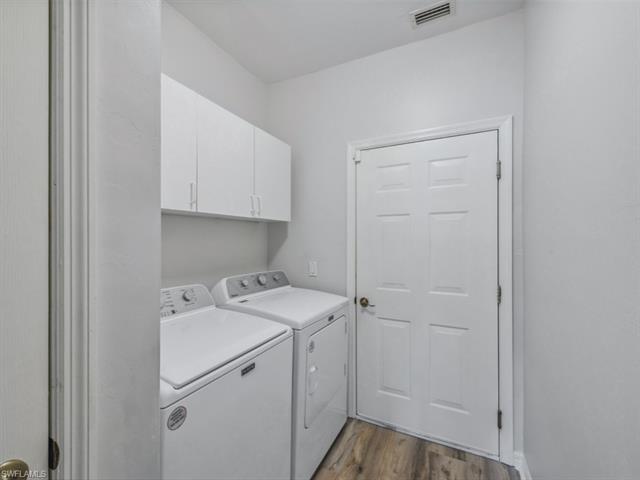 Washroom featuring visible vents, wood finished floors, washing machine and dryer, and cabinet space