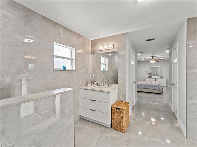 Full bathroom with connected bathroom, vanity, a ceiling fan, visible vents, and tile walls