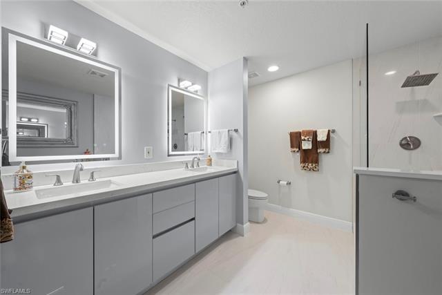 Bathroom featuring double vanity with quartz countertops, dual sinks, toilet, and a walk in shower, modern mirrors with touch screen controls.