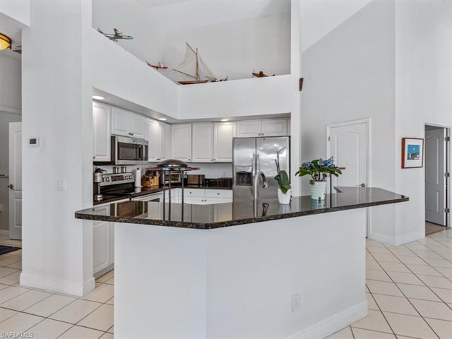 Kitchen featuring dark stone counters, a high ceiling, appliances with stainless steel finishes, and light tile patterned floors