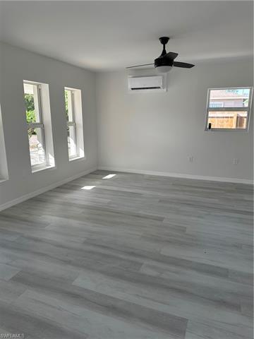 Living with a wall mounted air conditioner, baseboards, wood finished floors, and a ceiling fan