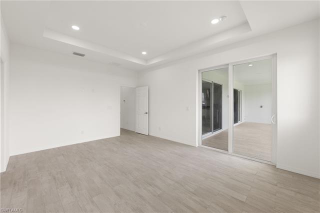 Unfurnished room with a tray ceiling, visible vents, light wood finished floors, and recessed lighting