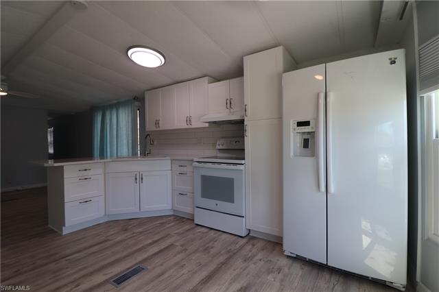 Kitchen with visible vents, a peninsula, white appliances, under cabinet range hood, and white cabinetry