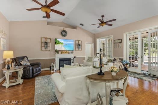 Living room with vaulted ceiling, a ceiling fan, wood finished floors, a glass covered fireplace, and visible vents