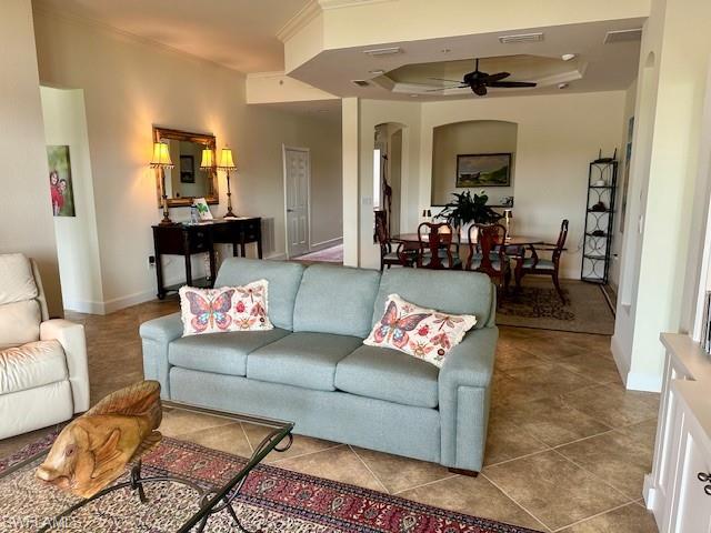 Tiled living area with a tray ceiling, a ceiling fan, visible vents, arched walkways, and ornamental molding