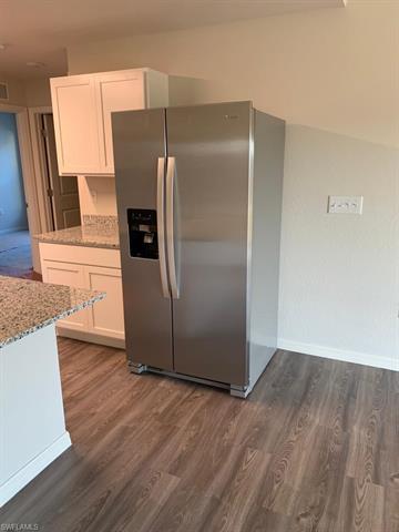 Kitchen with light stone counters, stainless steel fridge, dark wood-style floors, baseboards, and white cabinets