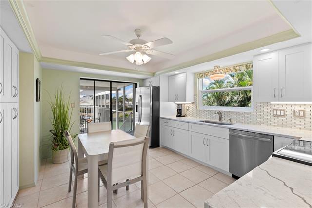 Kitchen with backsplash, a raised ceiling, a sink, light stone countertops, and stainless steel appliances