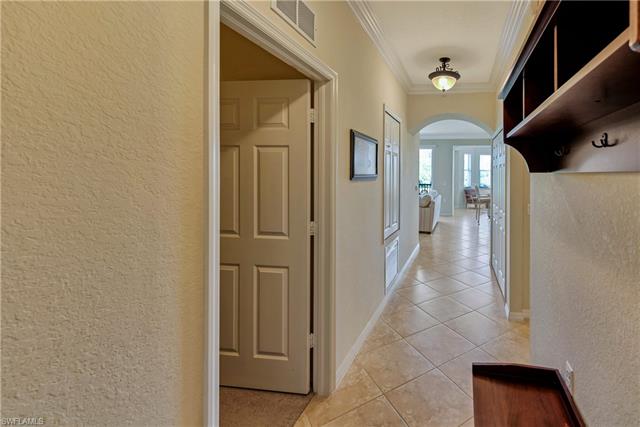 Hallway with light tile patterned floors, visible vents, arched walkways, ornamental molding, and a textured wall