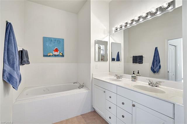 Full bath with double vanity, tile patterned flooring, a sink, and a  jetted tub